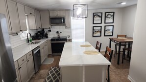 A modern kitchen with white cabinets, a central island, a microwave, and a dining area with a table and chairs. - Passing through/visiting family/doing business &need your own space? Stay Here! (Breckenridge)