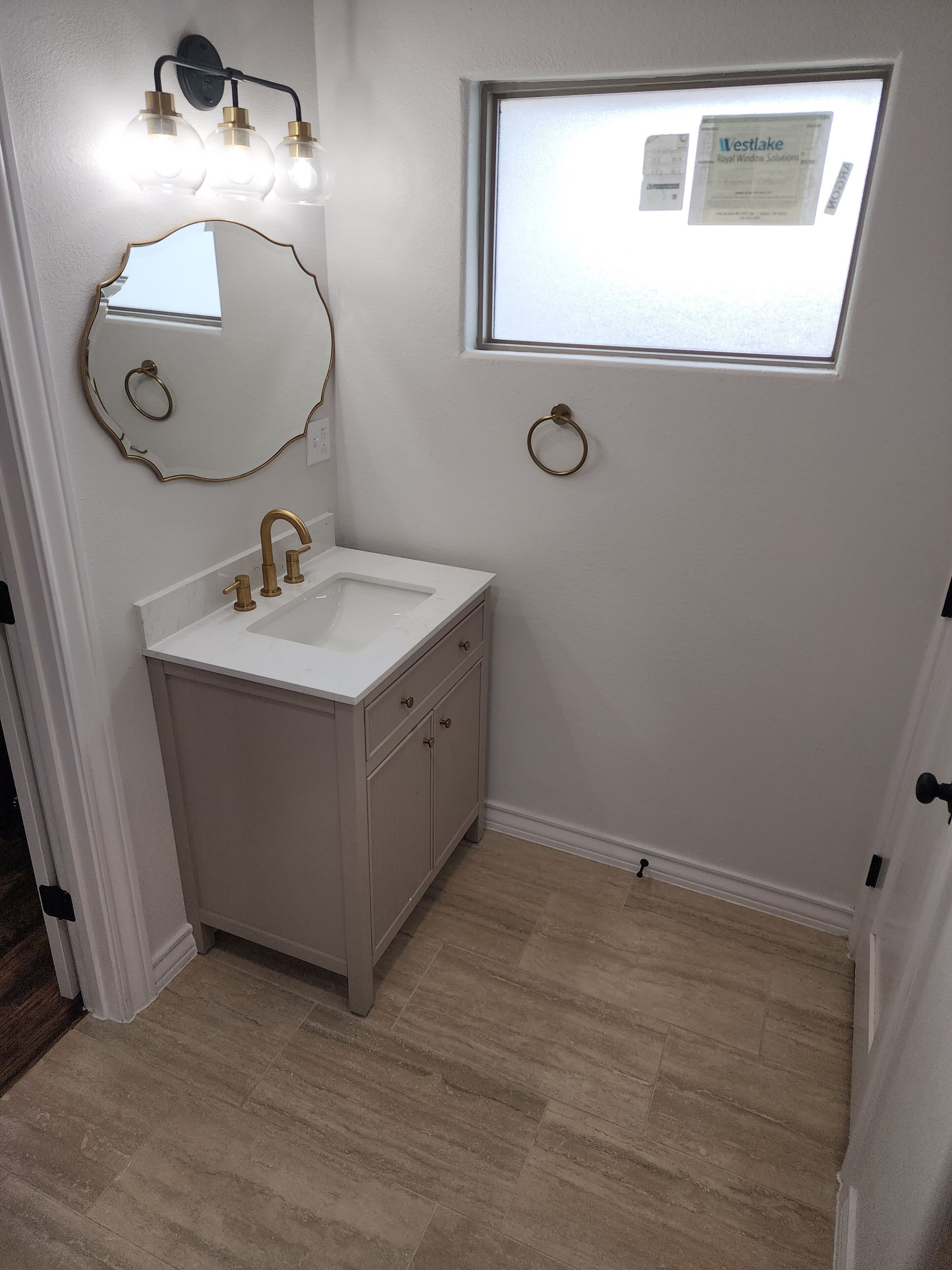 Un bagno con un mobile lavabo bianco, uno specchio con cornice dorata, una finestra che si affaccia sul cielo e un lampadario a parete.