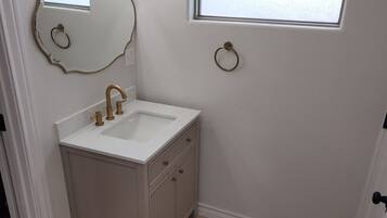 Un bagno con un mobile lavabo bianco, uno specchio con cornice dorata, una finestra che si affaccia sul cielo e un lampadario a parete.