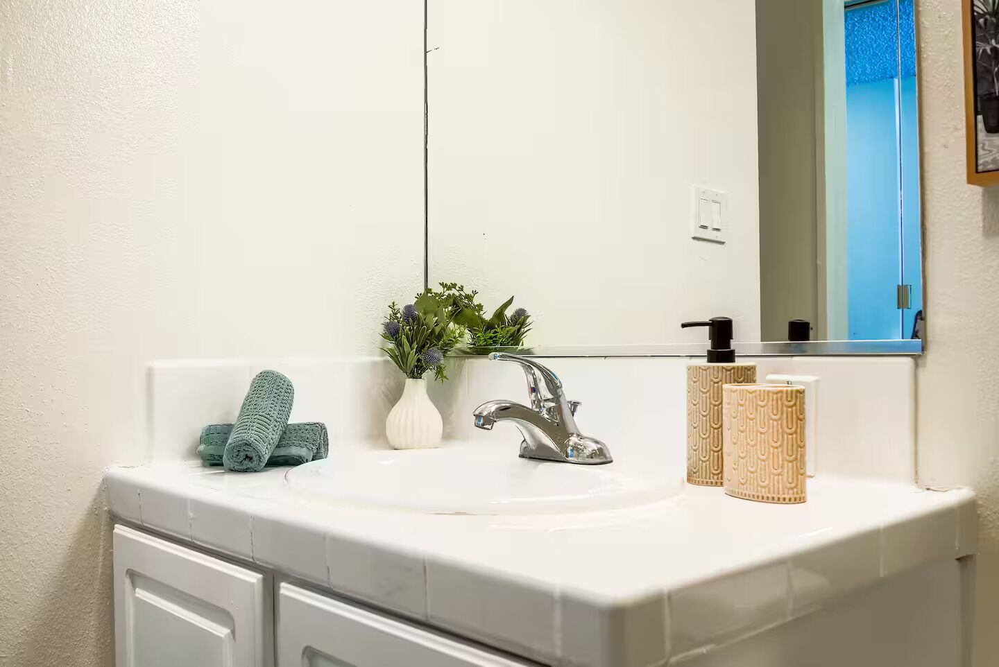 Un bagno con un lavandino bianco, un rubinetto argentato, uno specchio e una piccola pianta in vaso.