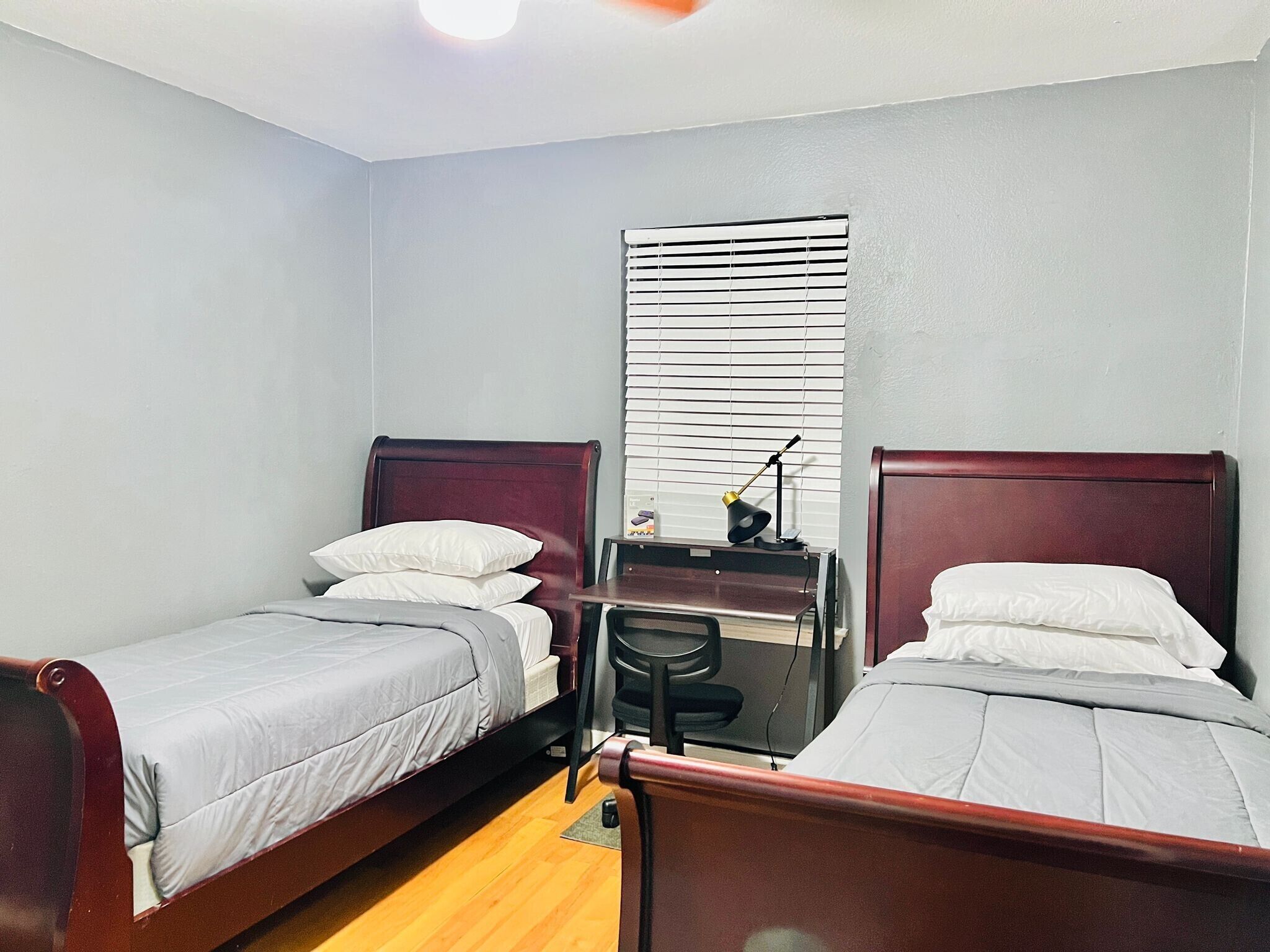 A small, clean room with two single beds, a desk, and a chair.
