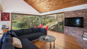 Una sala de estar moderna con techo de madera, ventanas amplias, chimenea de ladrillo y televisor de pantalla plana.