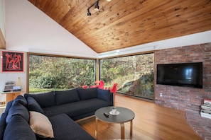 Una sala de estar moderna con techo de madera, ventanas amplias, chimenea de ladrillo y televisor de pantalla plana.