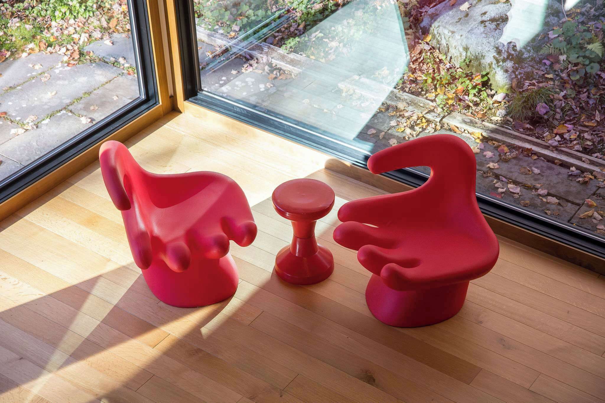 Une chambre moderne avec une grande fenêtre, un plancher en bois et deux chaises rouges.