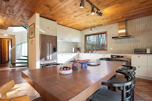 Una cocina moderna con techo de madera, armarios blancos y una isla grande con taburetes.