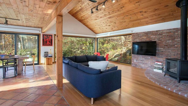Una sala de estar moderna con un sofá azul, techo de madera, ventanas grandes y una chimenea.