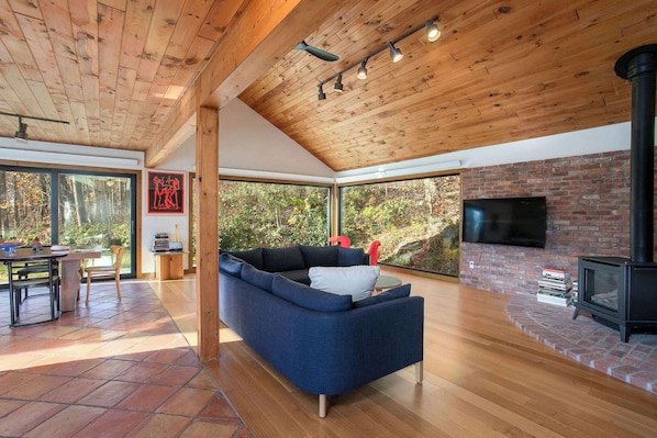 Una sala de estar moderna con un sofá azul, techo de madera, ventanas grandes y una chimenea.
