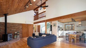 Amplia sala de estar con sofá azul, piso de madera, pared de ladrillo y una escalera que sube a un nivel superior.
