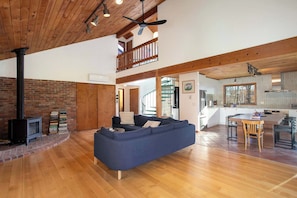 Amplia sala de estar con sofá azul, piso de madera, pared de ladrillo y una escalera que sube a un nivel superior.