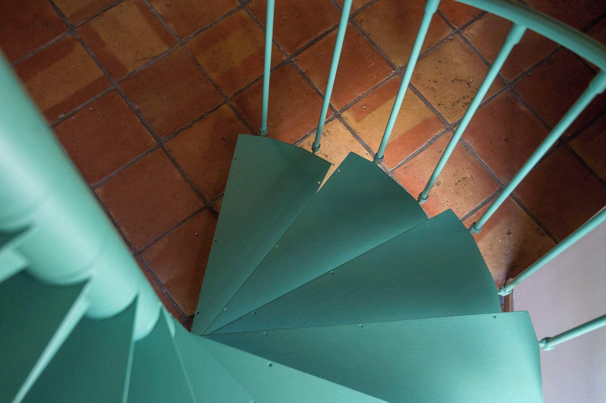 Un escalier en colimaçon avec des rampes en métal vert et un sol carrelé.