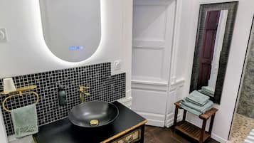 Une salle de bain avec un lavabo noir, un meuble-lavabo blanc, un miroir et un mur recouvert de carreaux.