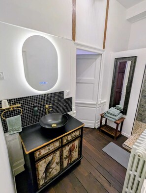 Une salle de bain avec un lavabo noir, un meuble-lavabo blanc, un miroir et un mur recouvert de carreaux.