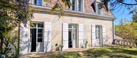 A two-story house with a brick facade, white shutters, and a garden with various plants.