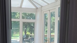 A conservatory with a wooden floor, large glass doors, and a view of a park. - Huge Home, Sleeps 24, Hot Tub, Pool Table (Harrisonville)