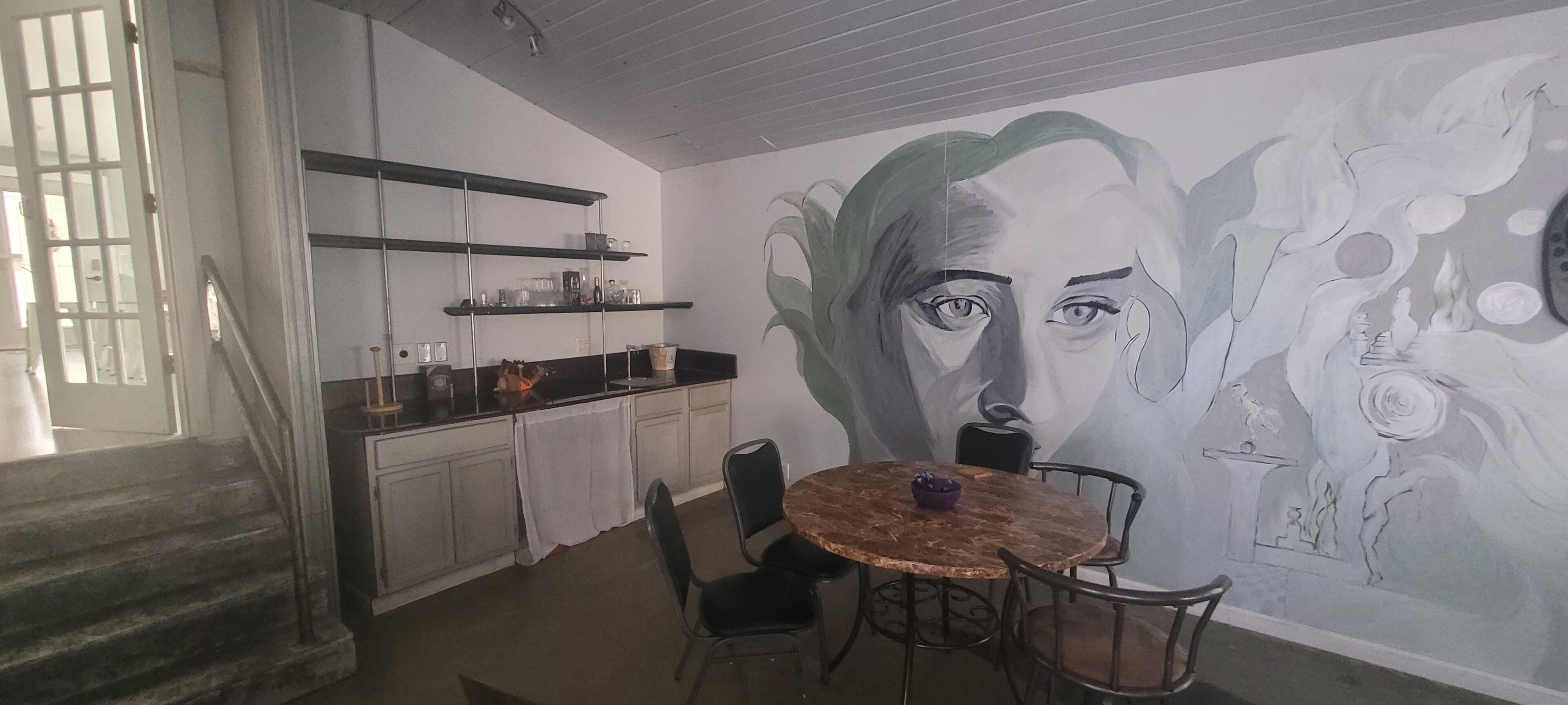 Zona pranzo con tavolo rotondo e sedie, un murale sulla parete e pensili della cucina sopra il bancone.