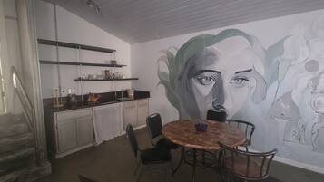Zona pranzo con tavolo rotondo e sedie, un murale sulla parete e pensili della cucina sopra il bancone.