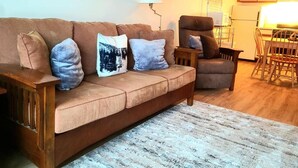 Ein Wohnzimmer mit einem braunen Sofa, einem Holzsesseln und einem gemusterten Teppich.