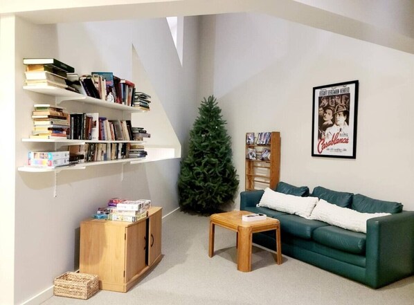 Una sala de estar con un sofá verde, una mesa de centro de madera, estanterías, un árbol de Navidad y un cuadro en la pared.
