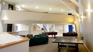 Ein geräumiges Zimmer mit Billardtisch, grünem Sofa und einer Spieltischtennisplatte.