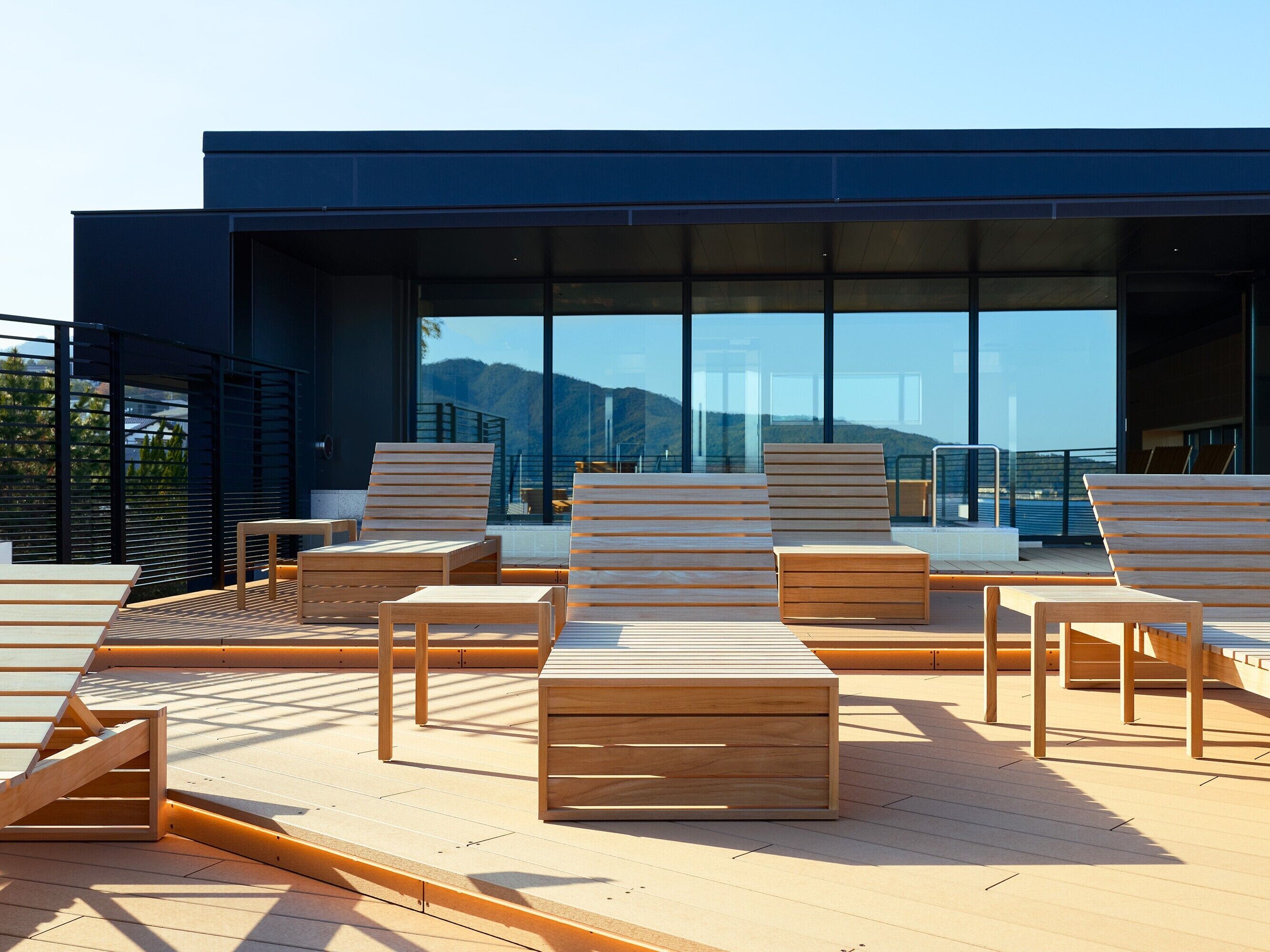 A modern outdoor lounge area with wooden furniture and large windows offering a view of the mountains.