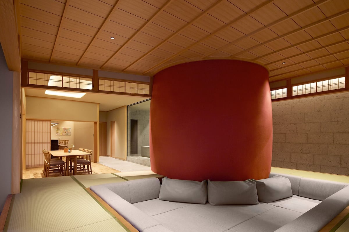 Ein traditionelles japanisches Interieur mit Tatami-Böden, einer niedrigen Holzbalkendecke und einem modernen Sofa mit Kissen.