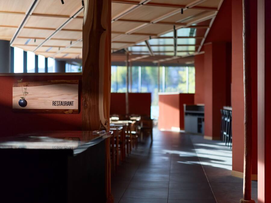 Interior de restaurante con mostrador de madera, un letrero que dice 'RESTAURANT' y vistas del exterior a través de grandes ventanales.