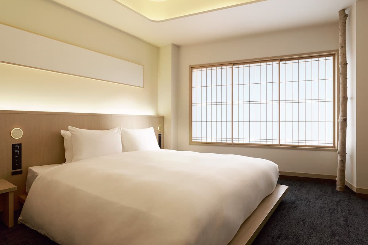 Ein Hotelzimmer mit einem großen Bett, einem Nachttisch, einem Fenster mit Blick und einer wandmontierten Bedienkonsole.