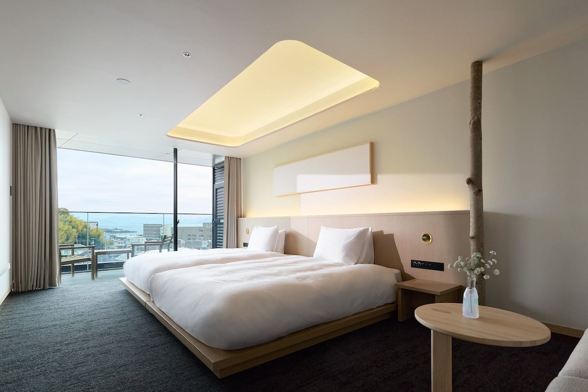 Ein modernes Hotelzimmer mit einem großen Bett, einem Nachttisch, einem kleinen runden Tisch, Blick auf die Stadt und einem Balkon.