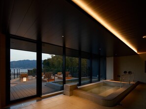 A modern spa with a large glass wall, a hot tub, and wooden deck furniture. - HOTEL FORK & KNIFE Miyajima (Hatsukaichi)