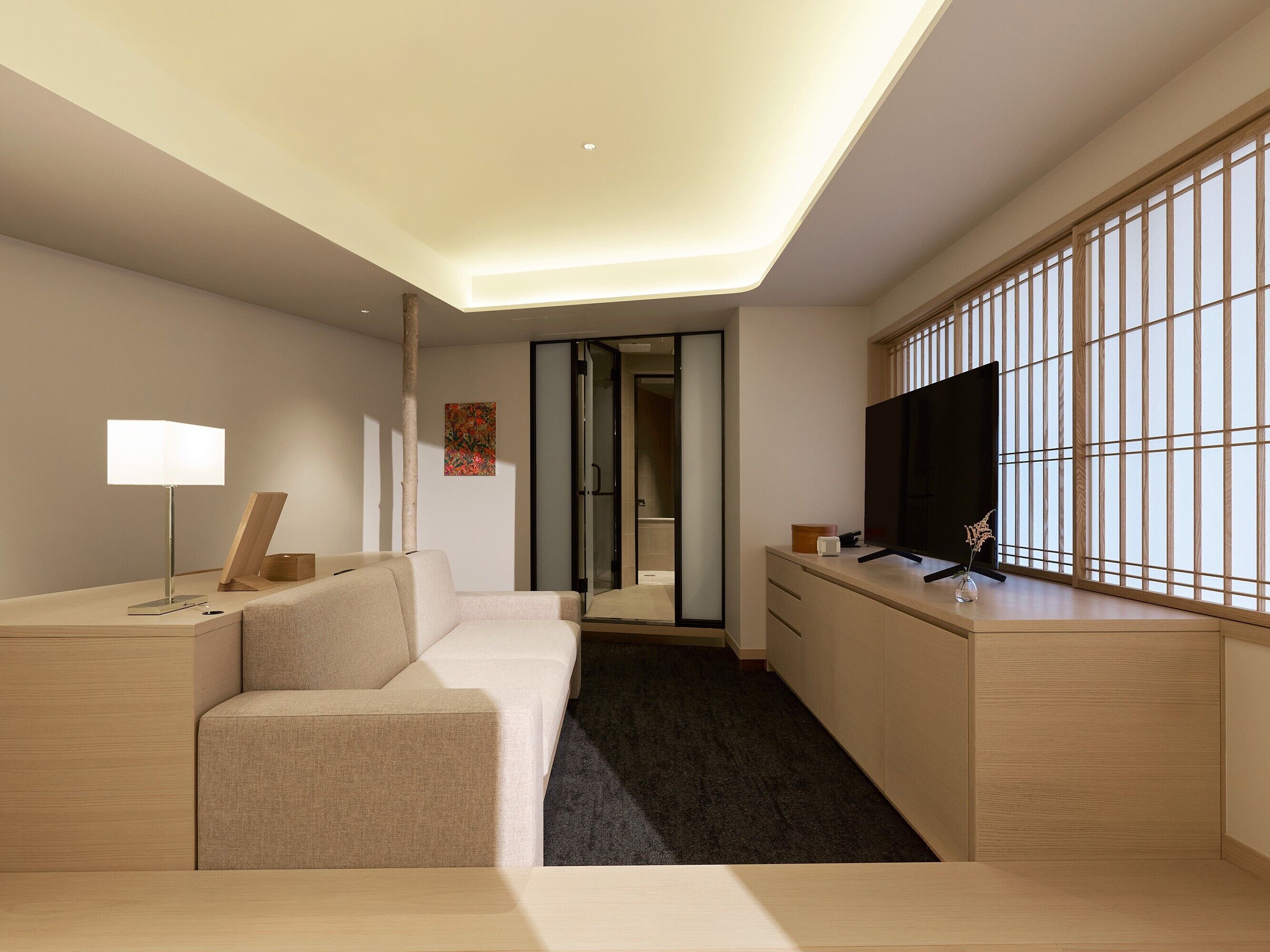 Een moderne hotelkamer met een bank, een bureau, een flatscreen-tv en een schuifdeur naar een badkamer.