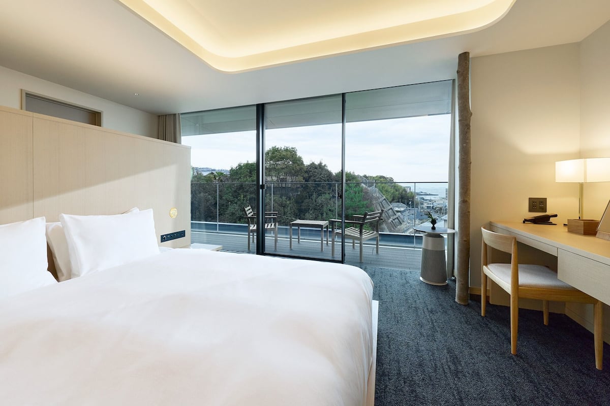 Ein Hotelzimmer mit einem großen Bett, einem Schreibtisch und einem Balkon mit Blick.
