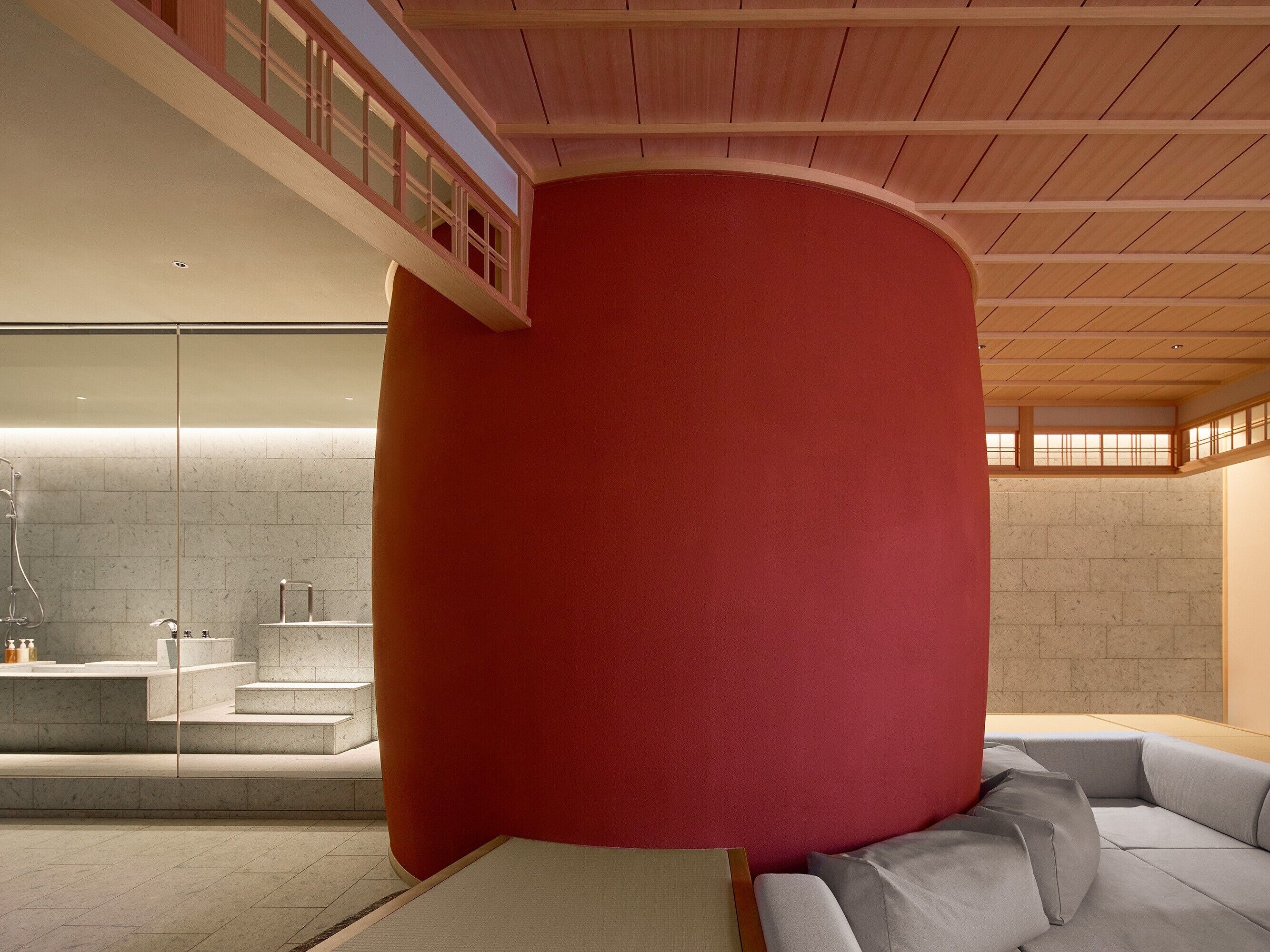A modern interior with a curved red wall, a grey sofa, and a bathroom with a glass shower.