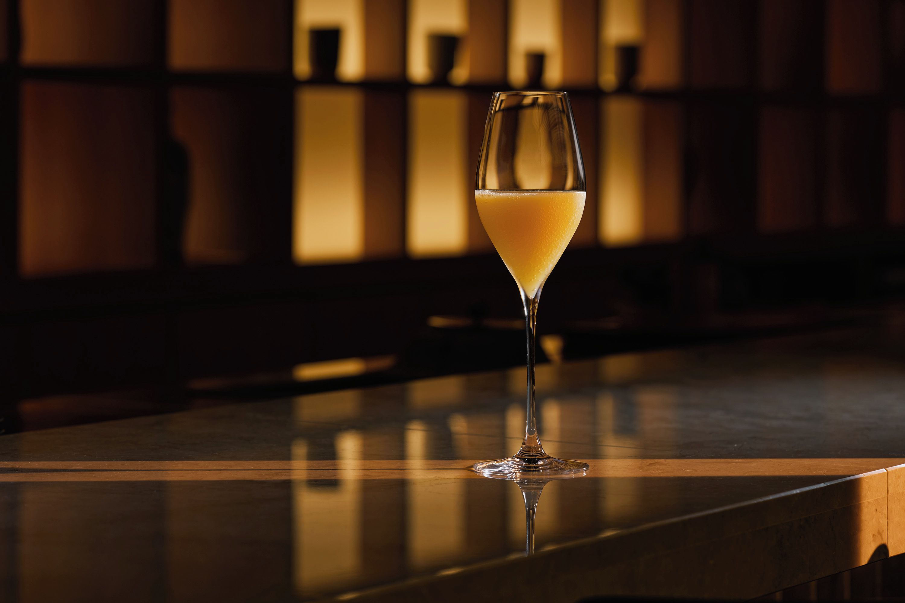 A glass of orange juice on a bar counter with a blurred background of shelves.