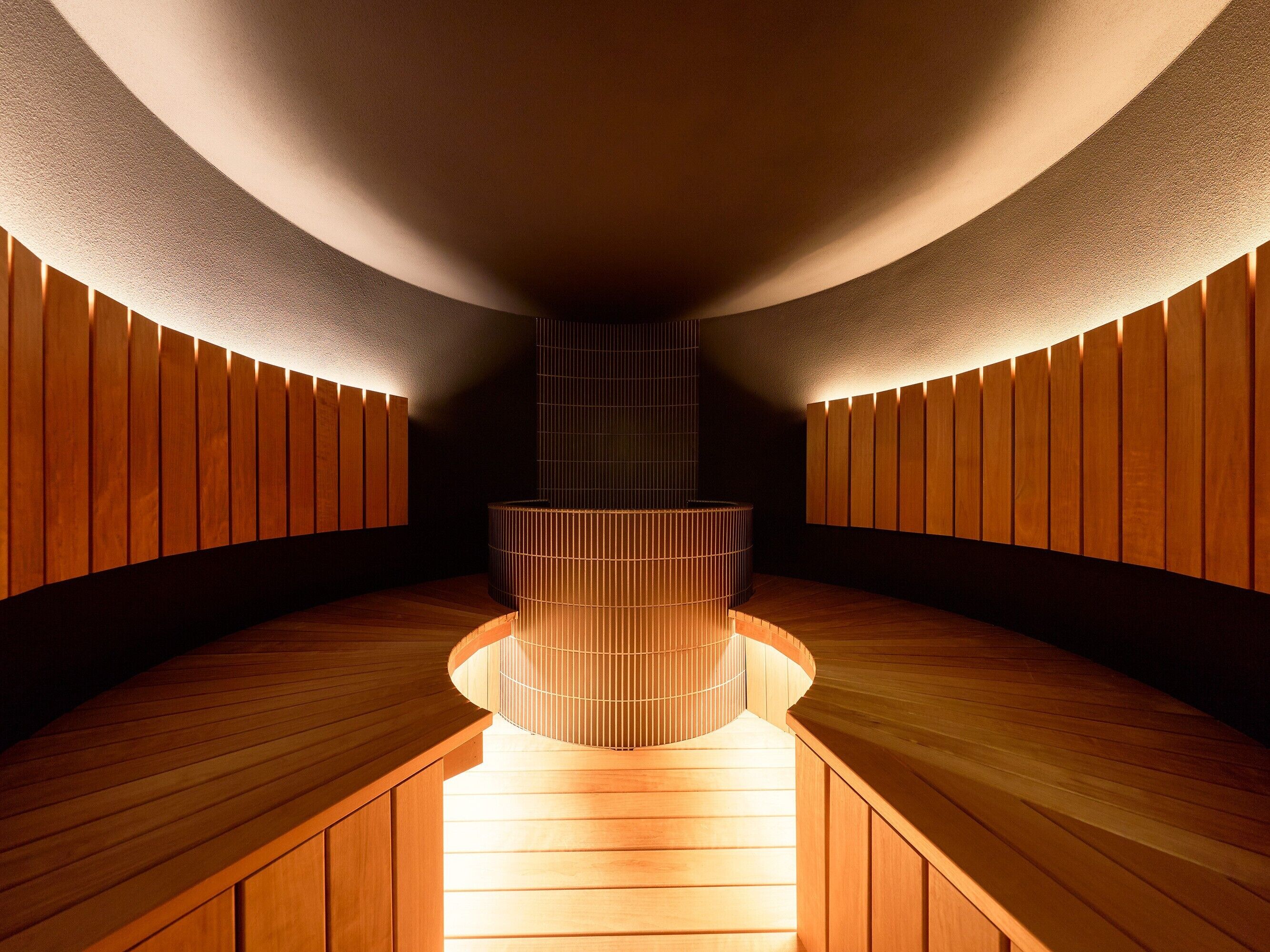 Un interior moderno con un banco curvo de madera, una columna central y paneles de madera en las paredes.