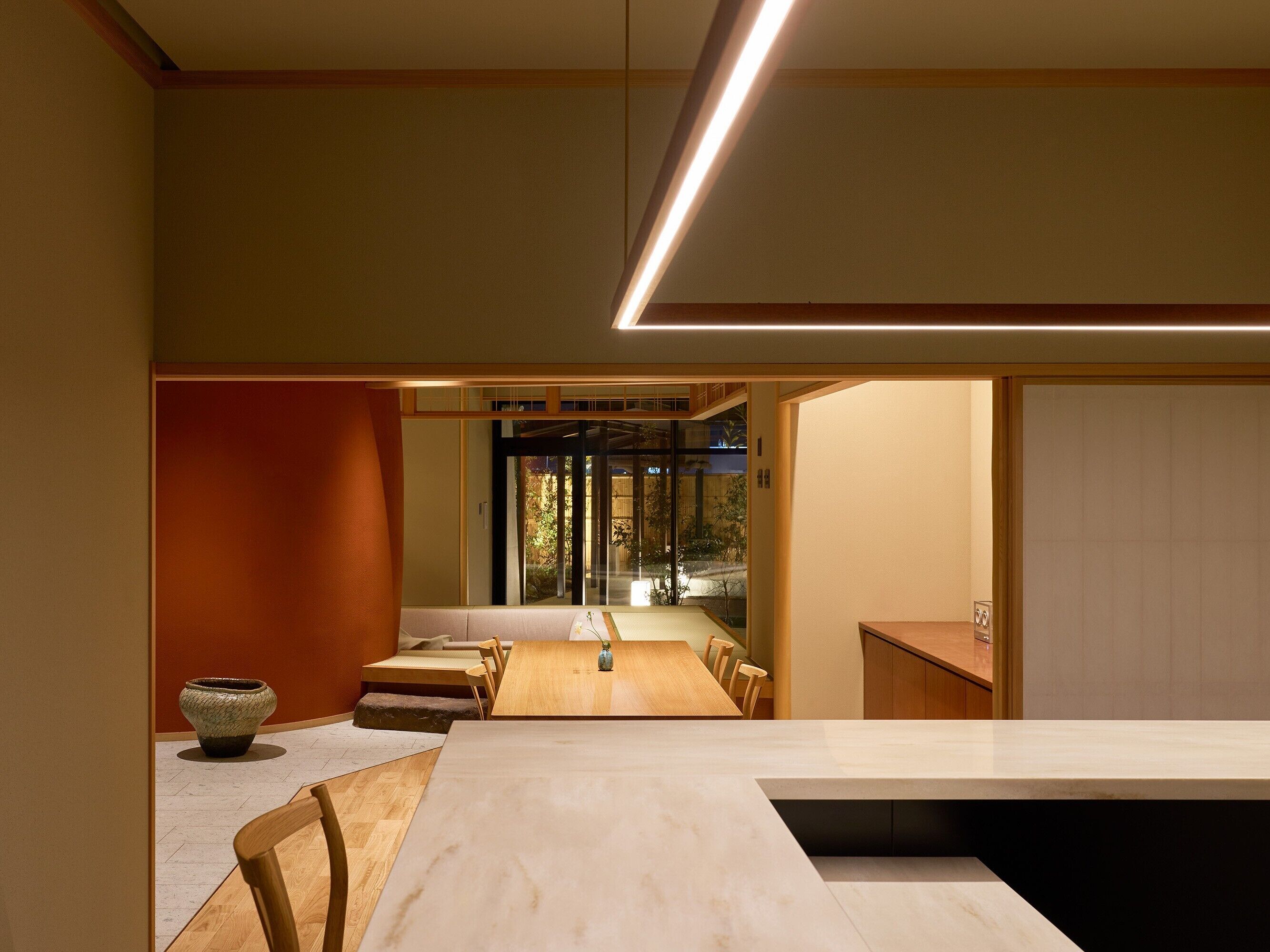 Un comedor moderno con una mesa larga, sillas de madera y un florero.