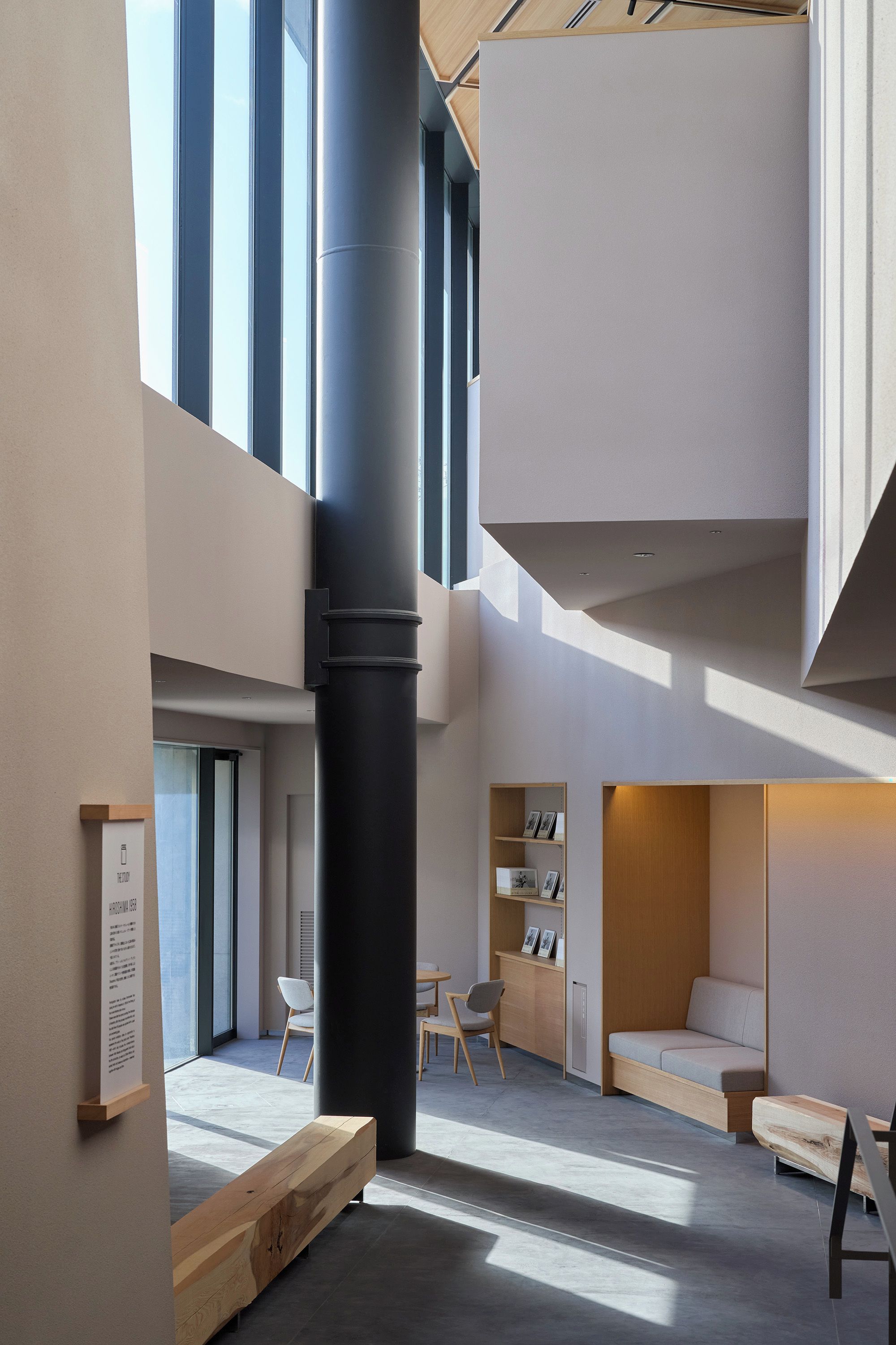 A modern interior with a high ceiling, a central black column, and a seating area with a sofa and chairs.