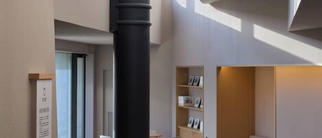 A modern interior with a high ceiling, a central black column, and a seating area with a sofa and chairs.