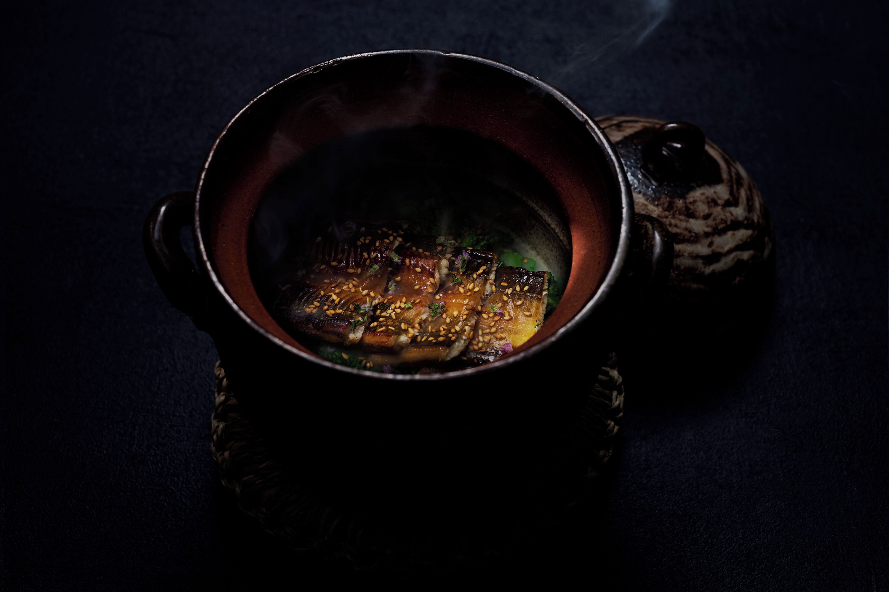 A ceramic mug with a handle, containing a steaming beverage, placed on a dark surface.