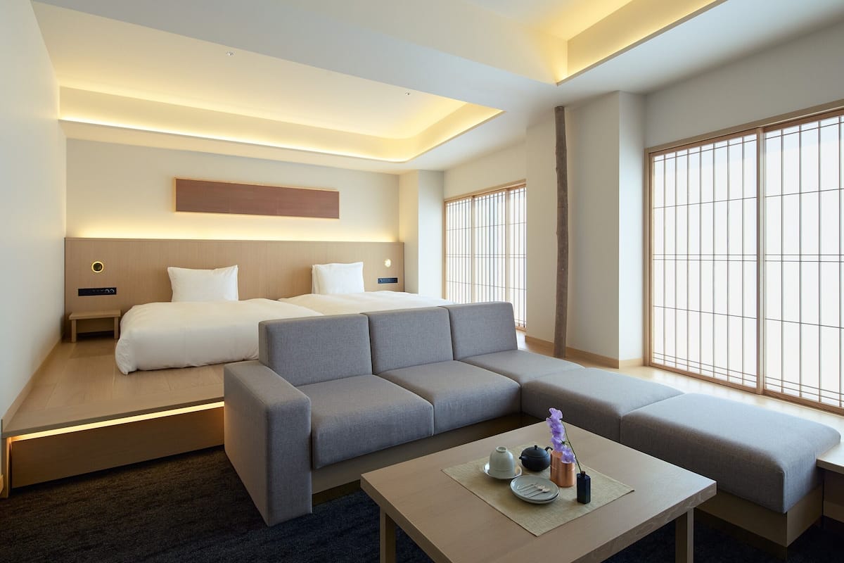 Ein modernes Hotelzimmer mit einer Couch, zwei Betten, einem Couchtisch und Blick auf die Stadt.