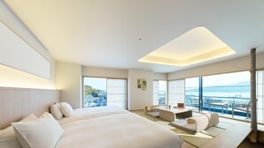 A modern hotel room with a large bed, a seating area, and a view of the city. - HOTEL FORK & KNIFE Miyajima (Hatsukaichi)