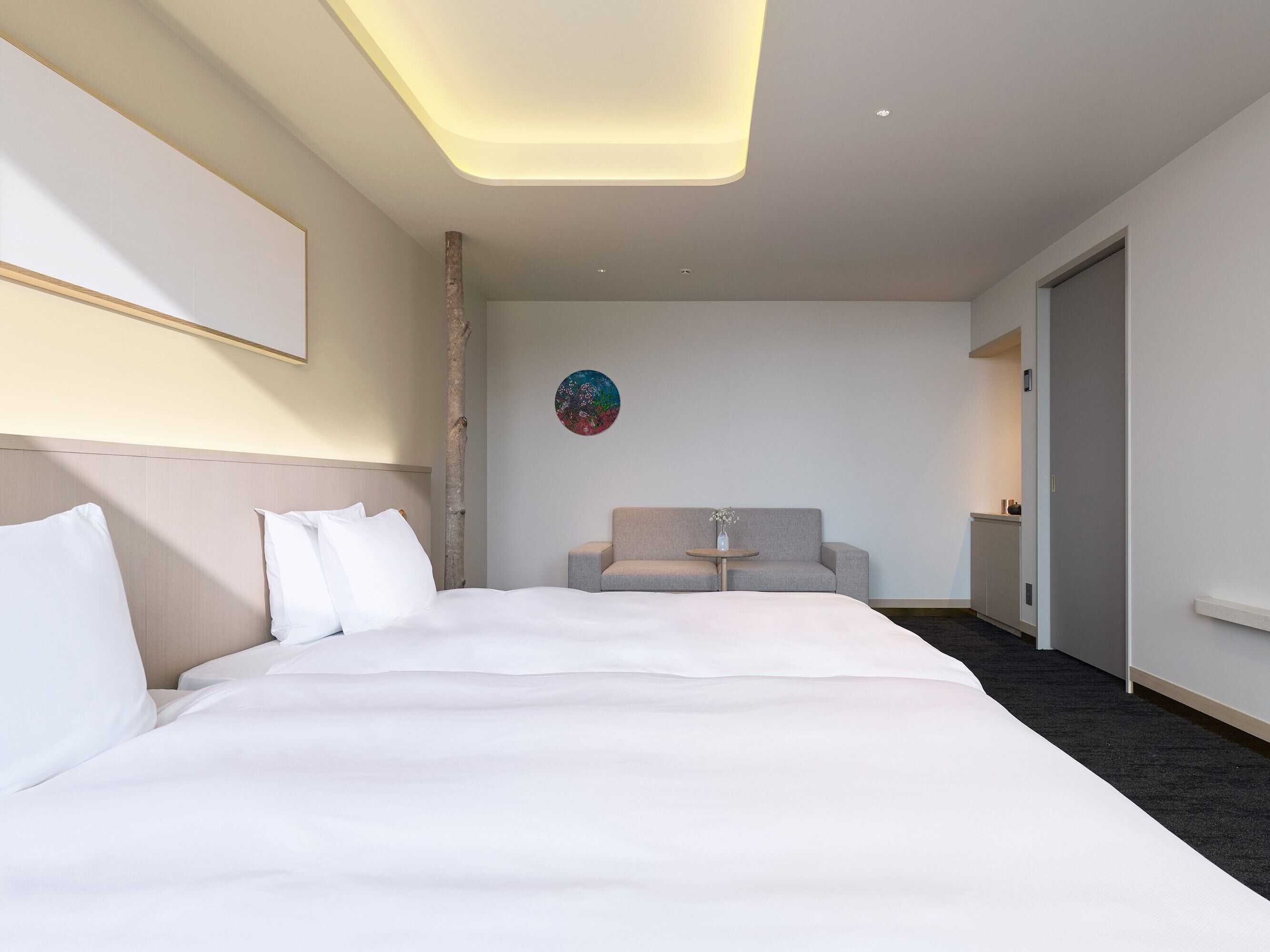 A hotel room with a large bed, a sofa, a small table, and a painting on the wall.