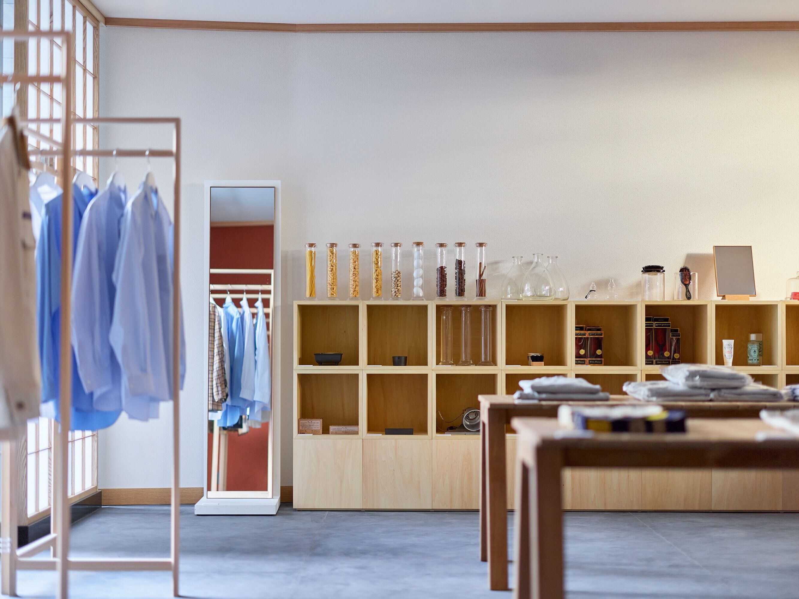 A room with a wooden wardrobe, shelves with various items, and a table with folded clothes.