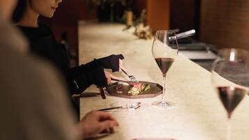 A dining table with a plate of food, a glass of red wine, and a person using cutlery.
