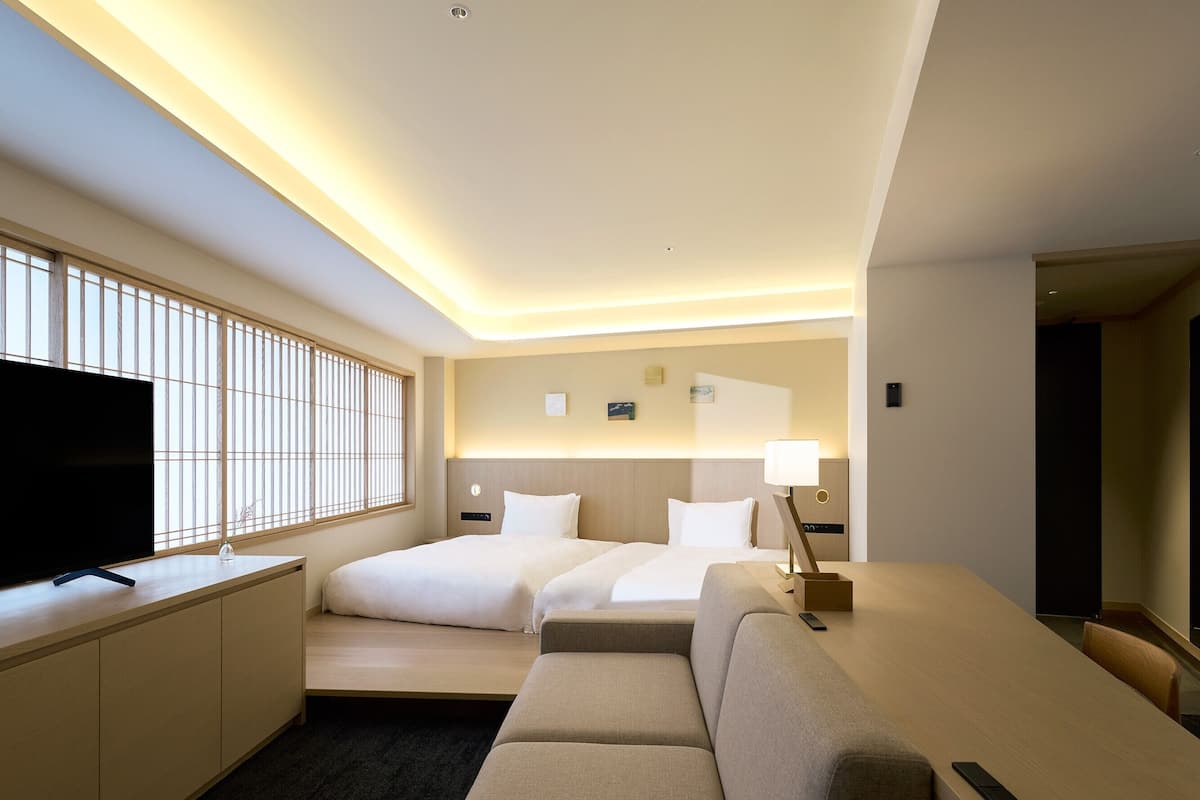 Ein Hotelzimmer mit Fernseher, zwei Betten, einer Sitzecke und einem Schreibtisch.