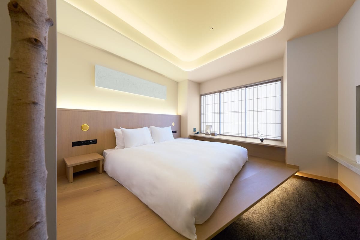 Ein modernes Hotelzimmer mit einem großen Bett, einem Nachttisch, einem Fenster mit Gitterstäben und einem Wandbild.