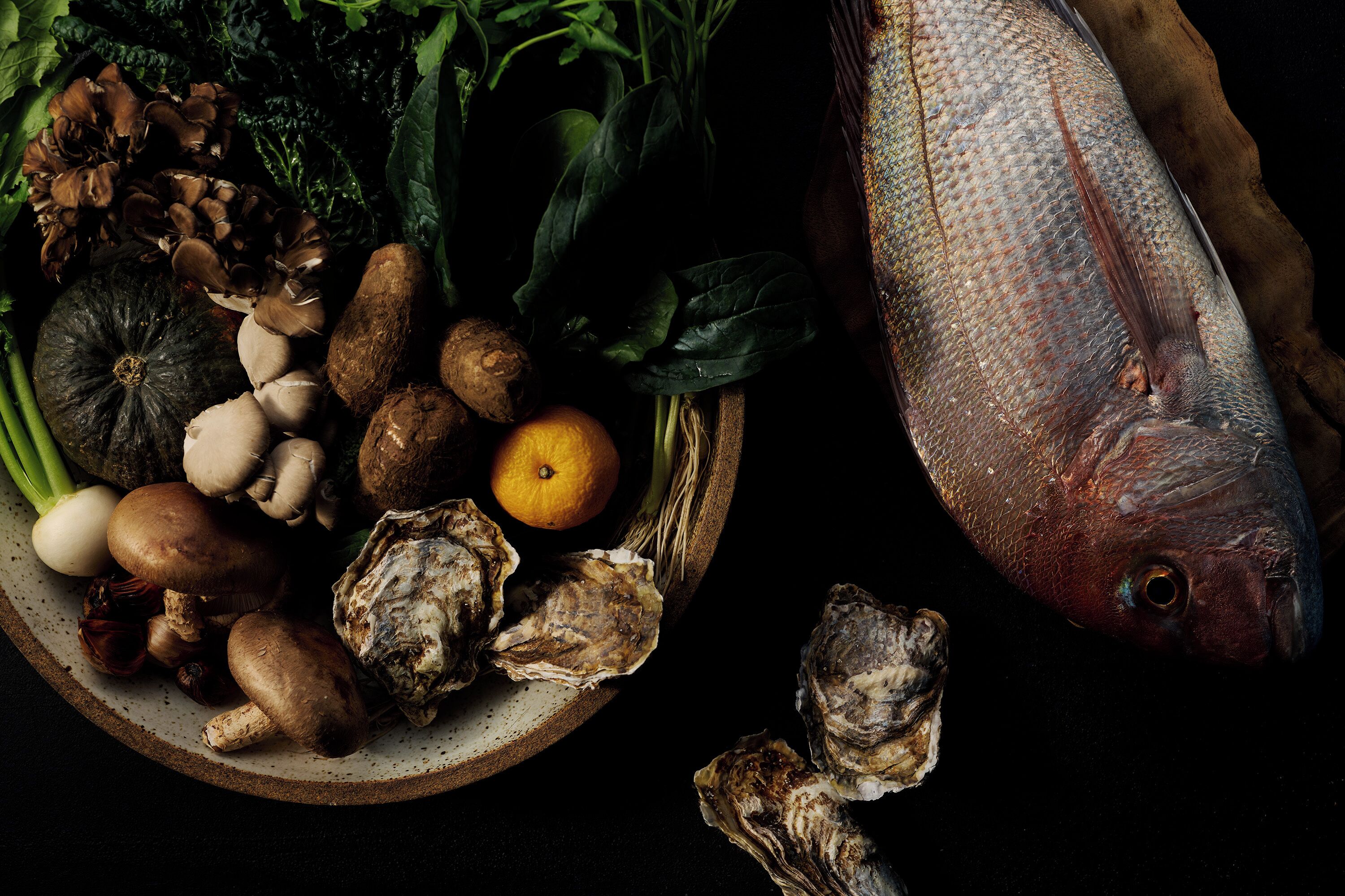 A variety of seafood and vegetables on a plate, including oysters, mushrooms, and a fish.