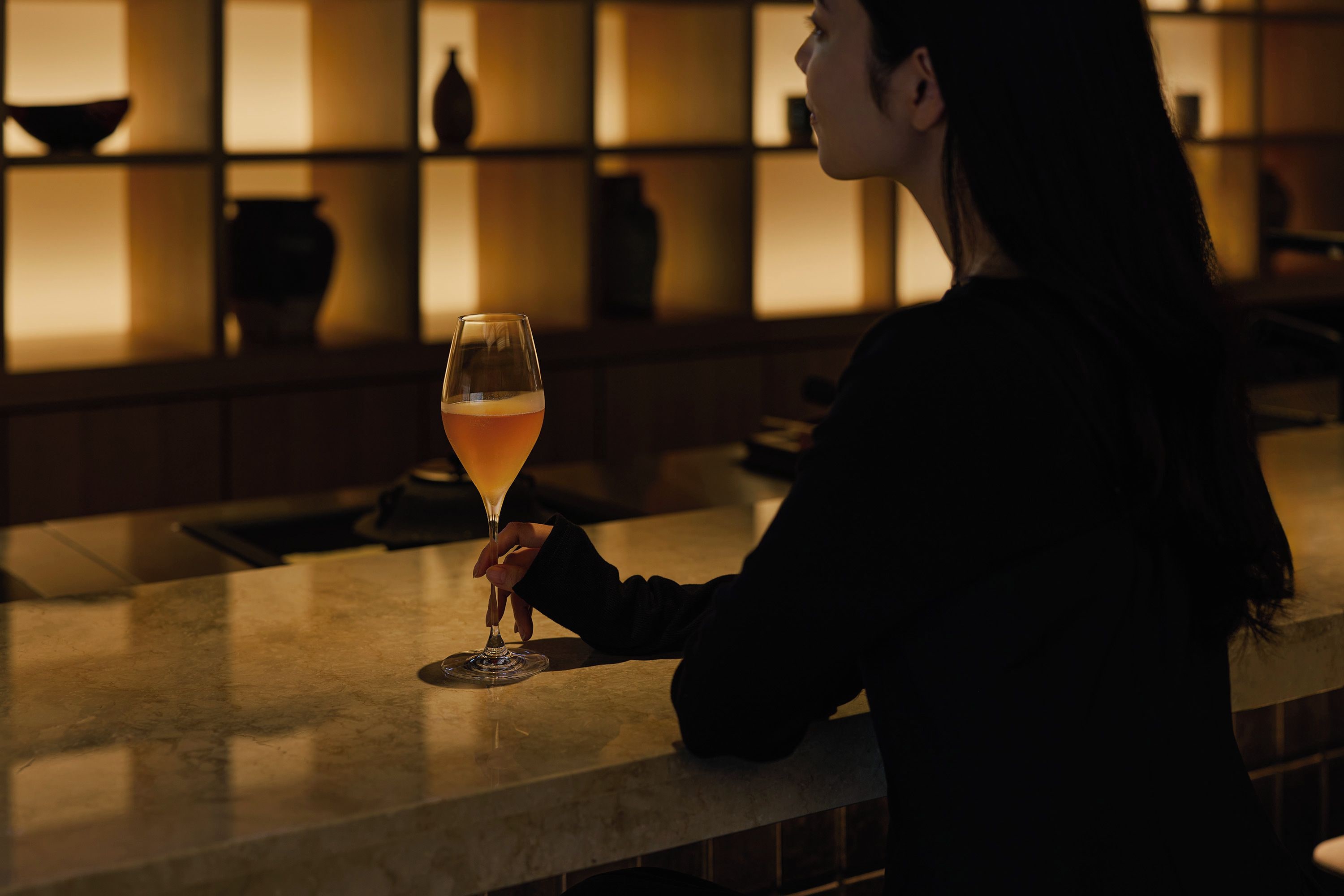 A person holding a glass at a bar with a tiled backsplash.