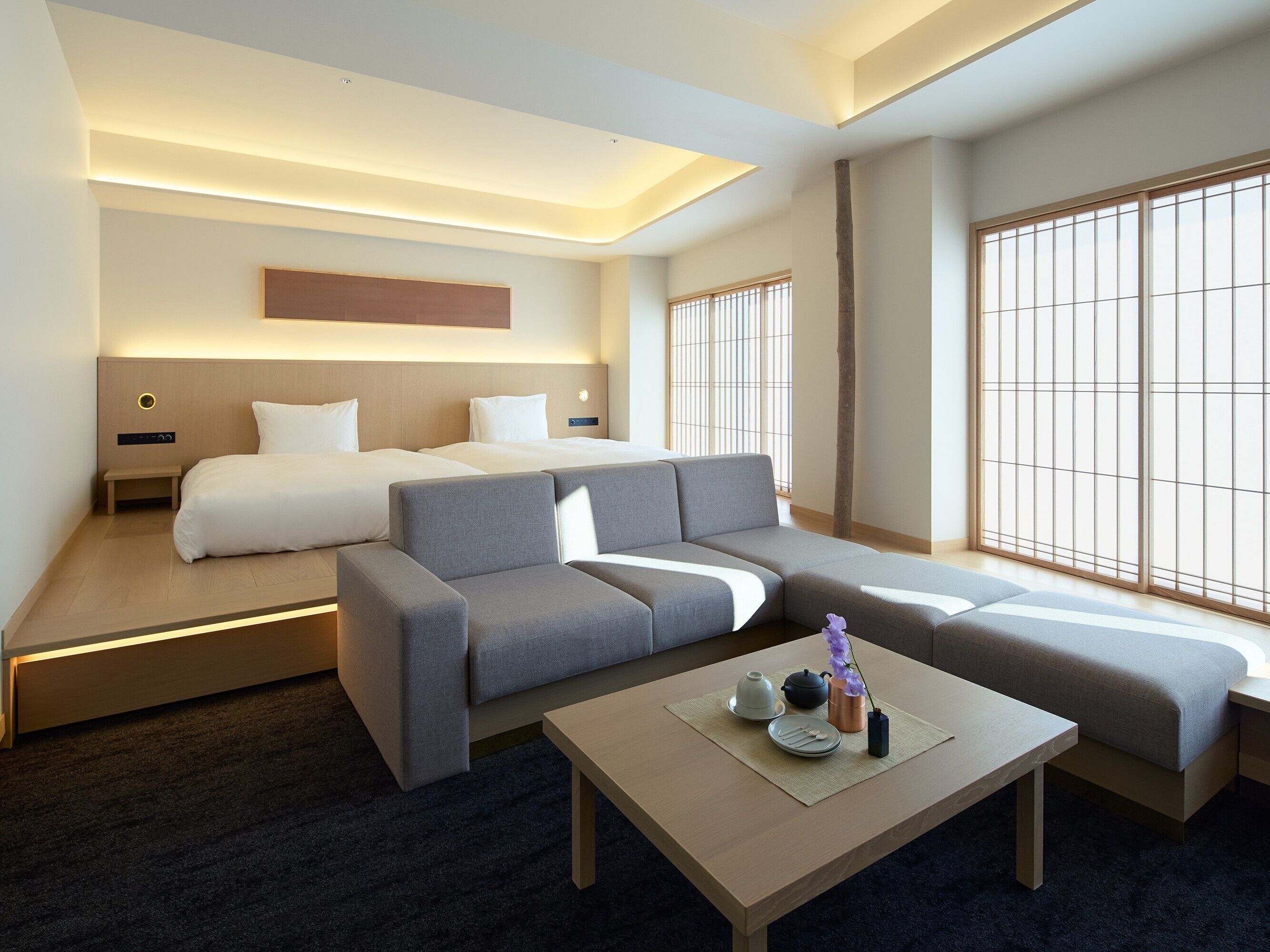 A modern hotel room with a sofa, a bed, a small table with tea set, and large windows.