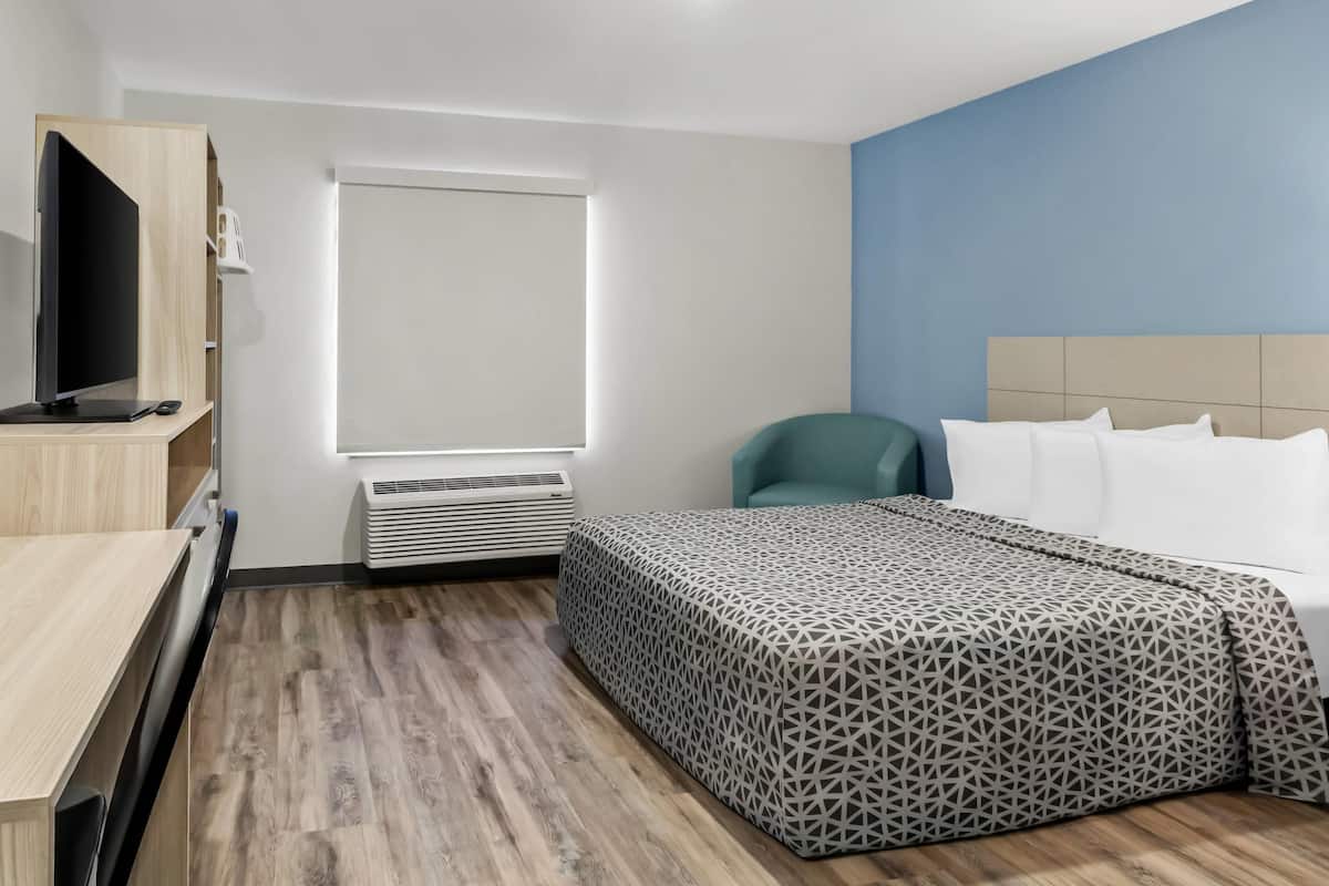 A hotel room with a bed, a desk, a television, a window, and an air conditioning unit.