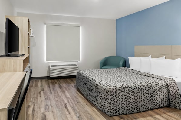A hotel room with a bed, a desk, a television, a window, and an air conditioning unit. - WoodSpring Suites Washington Meadowlands PA (Washington)